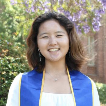 Allyson Kang stands in the middle of the frame, facing the camera and smiling.