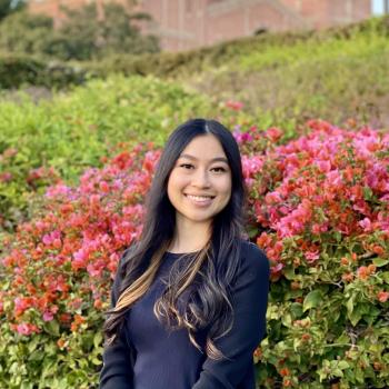 Carolyn Ta stands in the middle of the frame, facing the camera and smiling. 