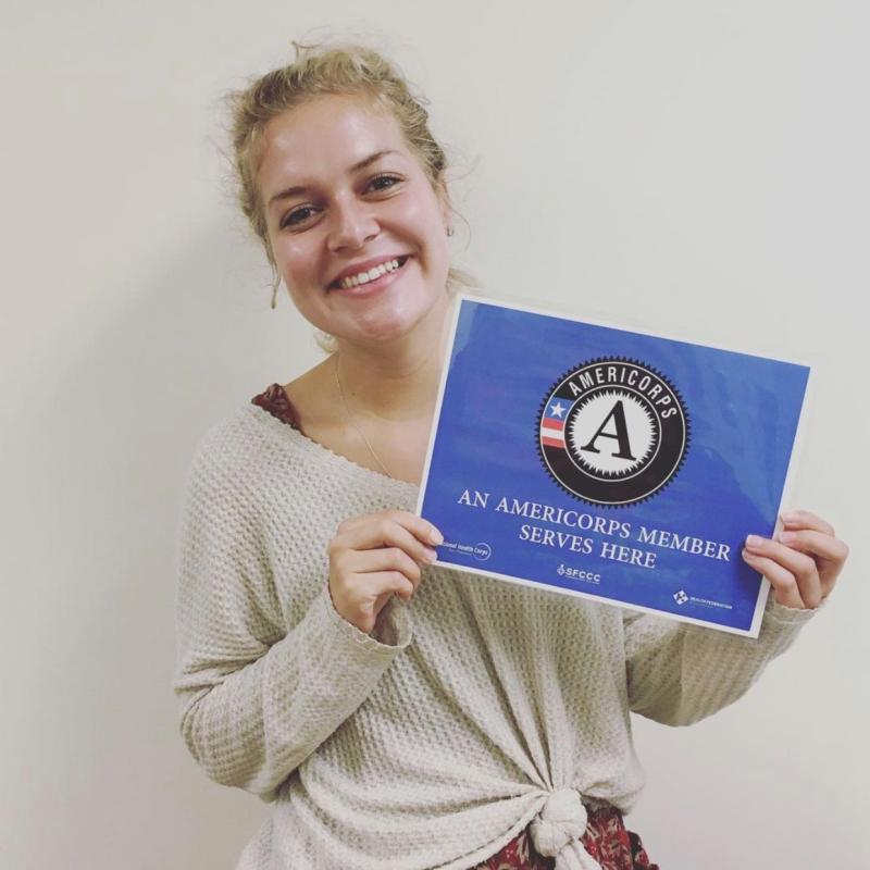 Lauren Hall holding an "AmeriCorps member serves here" sign at Curry Senior Center.