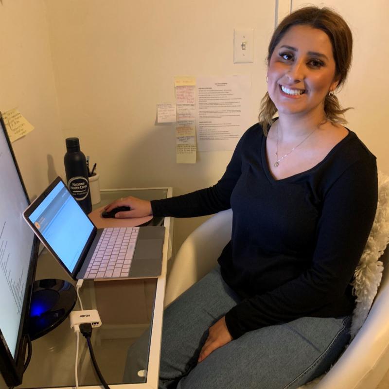 Evelyn De Arcos sitting in a comfy white chair, in front of her computer and monitor, while she serves from home.