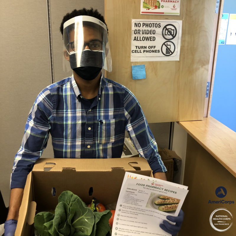 NHC SF Member Spencer Robinson holding a box of produce and a recipe for patients at Food Pharmacy.