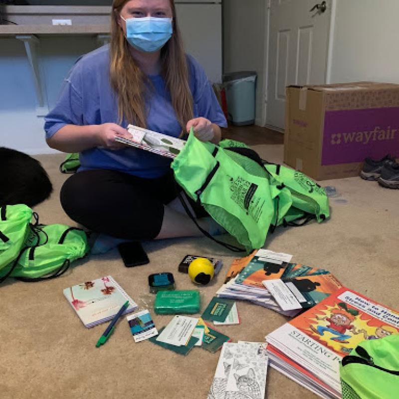 NHC member Paige sitting on the floor filling green bags with items called wellness kits