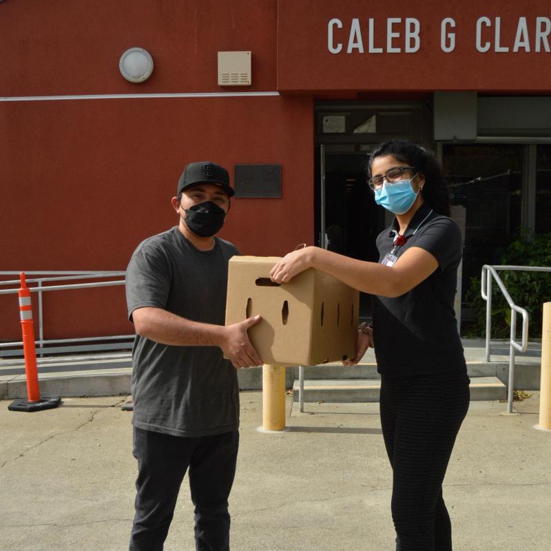 Saadhana Deshpande (right) holding a box of produce together with M. O. (left), one of the drivers for one of the produce delivery companies that aids the FAMC.