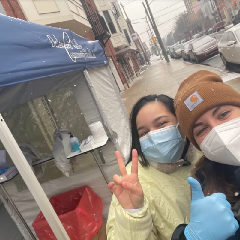 two people with masks on in front of a covid testing tent on a snowy day