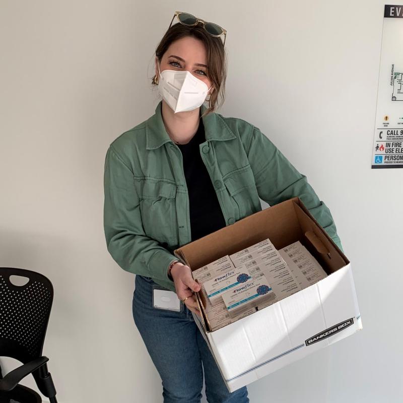 Vjola Jorgji is facing the camera directly. She is wearing a facmask. She is holding a box with Rapid COVID-19 tests to be distributed to patients.