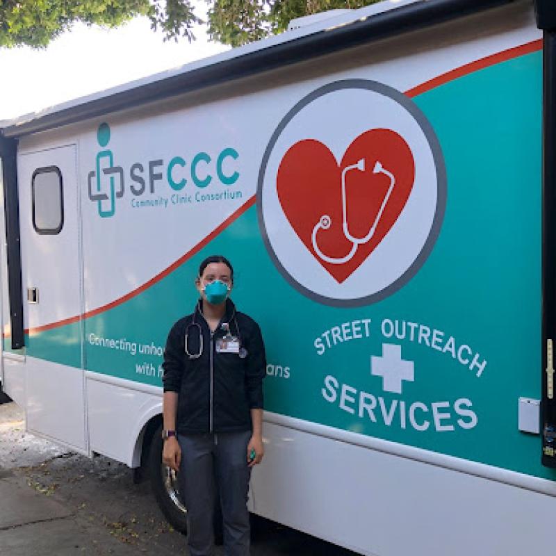 A person stands in front of a mural that reads "SFCCC" in the upper left-hand corner and "Street Outreach Services" in the lower right corner.