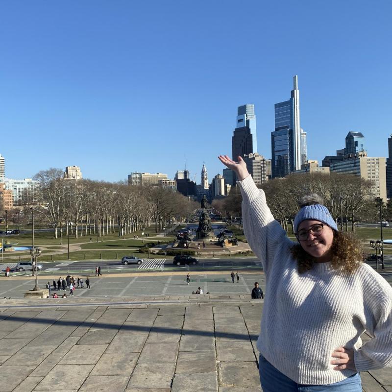 Emily standing on the "Rocky Steps" with the Philadelphia skyline in the background