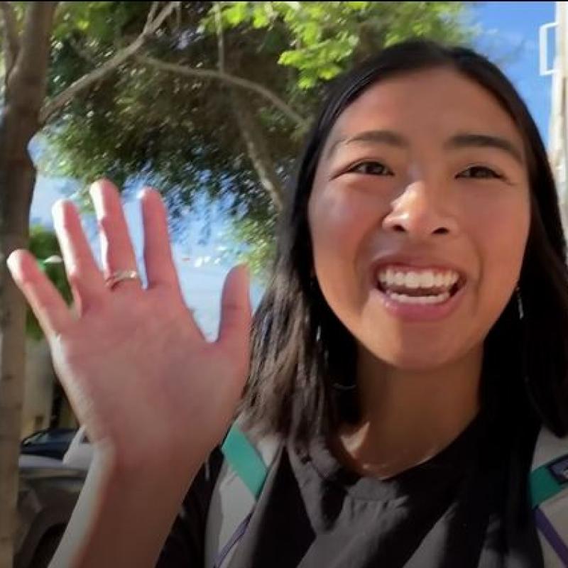 A person is facing the camera and smiling while waving at the audience.