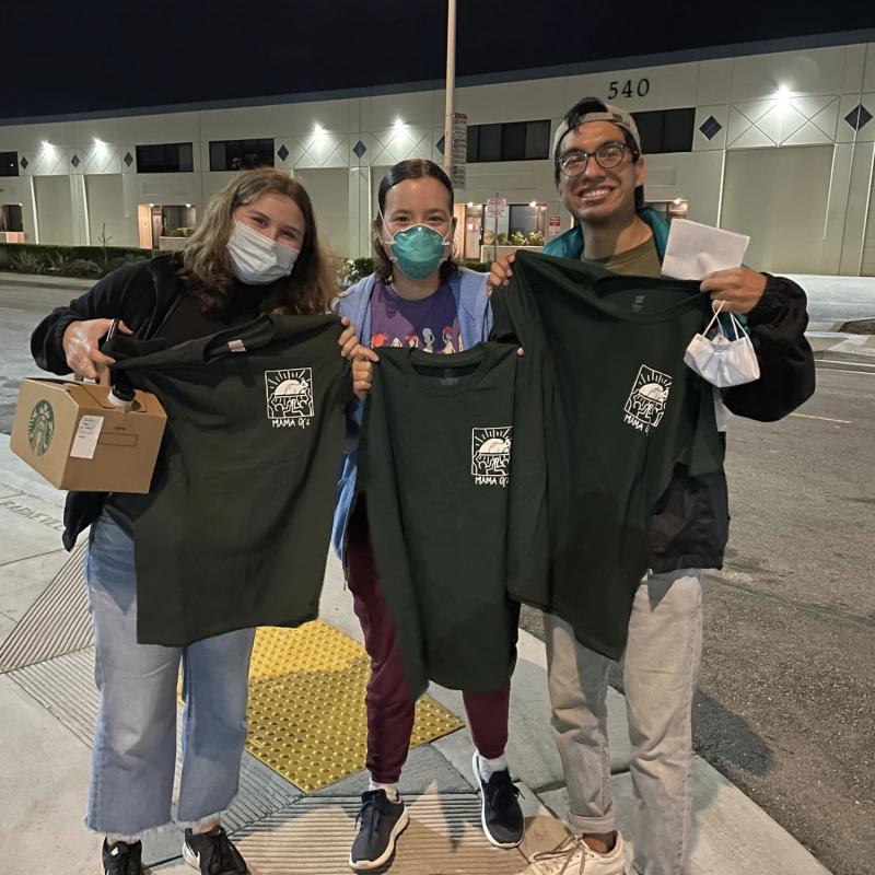 three people stand in the center of the frame, holding up t-shirts 