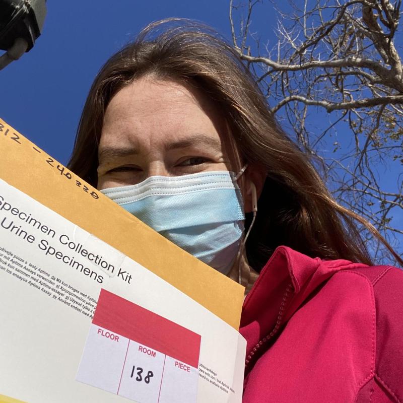 Catherine is seen here taking a selfie during service. She is holding a box marked with a label that says urine samples. 