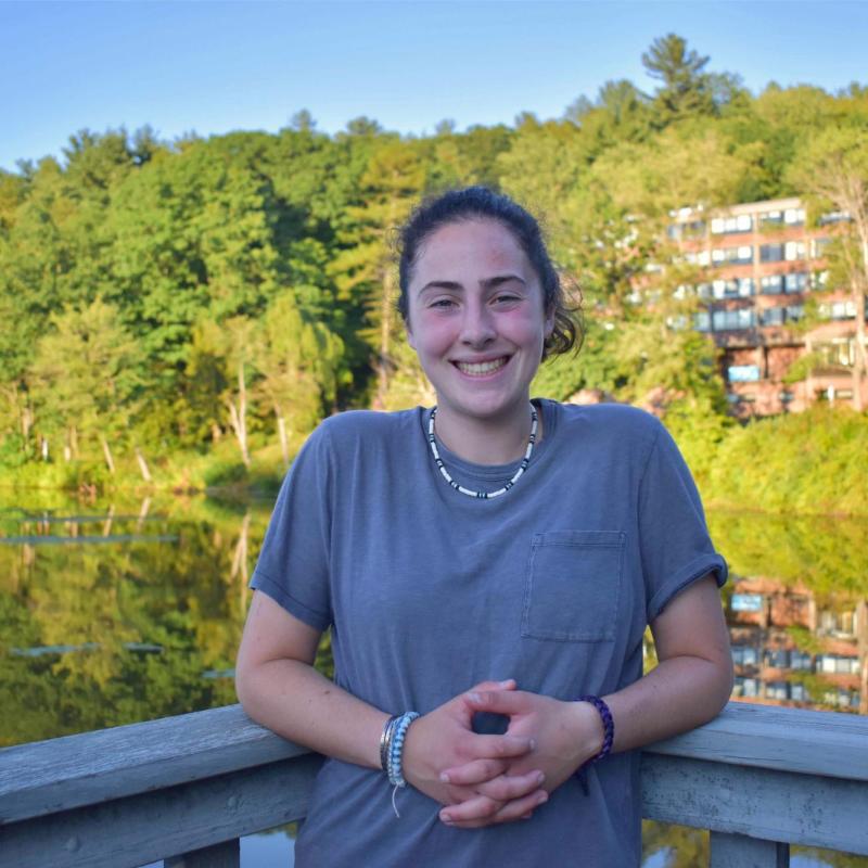 Lilly stands in front of a lake with trees.