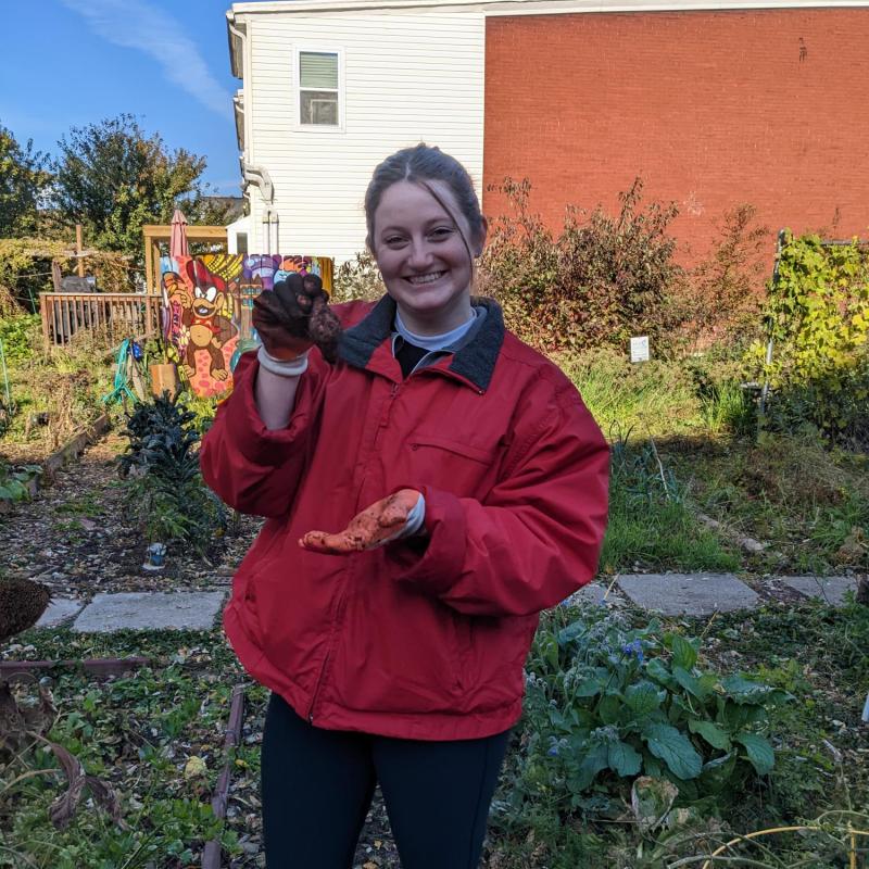 Shannon is standing in a garden holding a vegetable.
