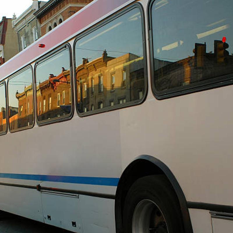 the side of a bus with row homes showing in the reflection of the windows