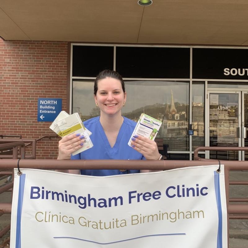 Aurelia is sitting behind a Birmingham Free Clinic sign.