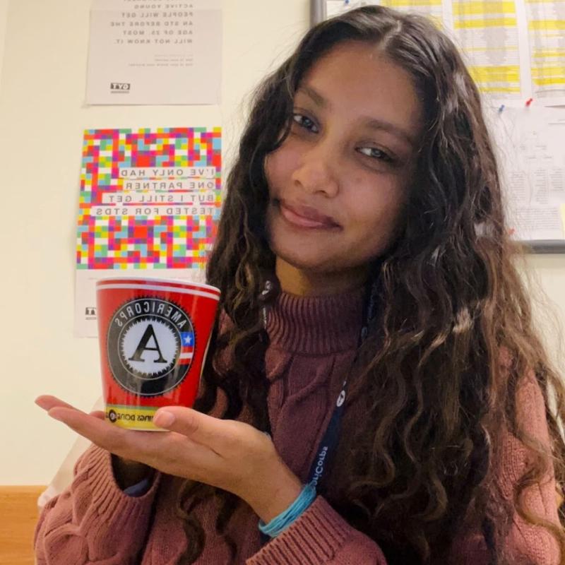 Aneesha holding a mug with the AmeriCorps logo on it