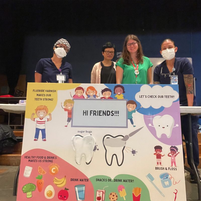 Emily standing with her colleagues behind a poster advocating for practices that help maintain healthy teeth for children. 