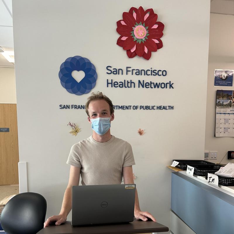 John Hansen is standing and facing the camera. Behind them is the San Francisco Health Network logo. 