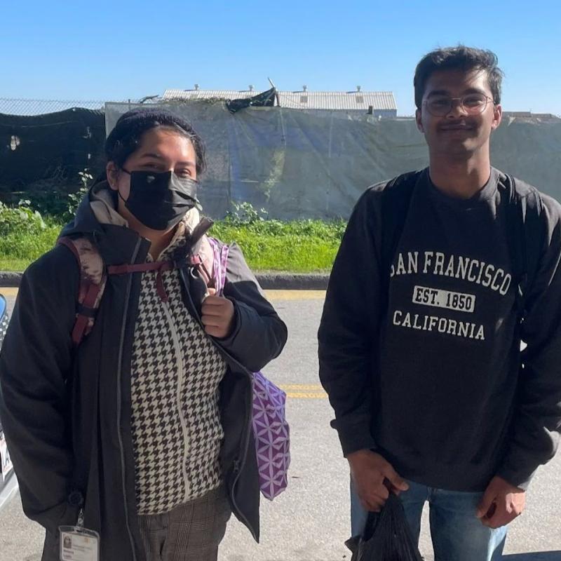 AmeriCorps members Melanie Lopez (left) and Shreyas (right) stand in the center of the frame, facing the camera and smiling. 