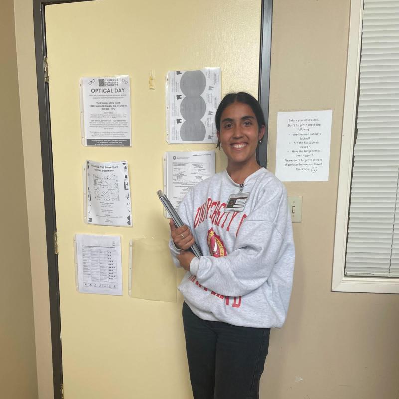 Anjalie is off-center of the frame, facing the camera and smiling. She is holding a resources binder. 