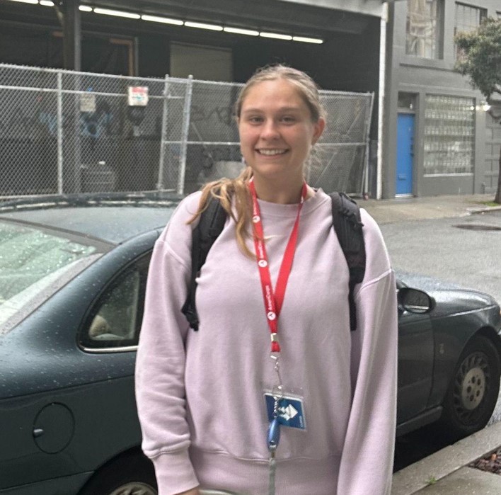 Hannah is standing in the middle of the frame, facing the camera and smiling.